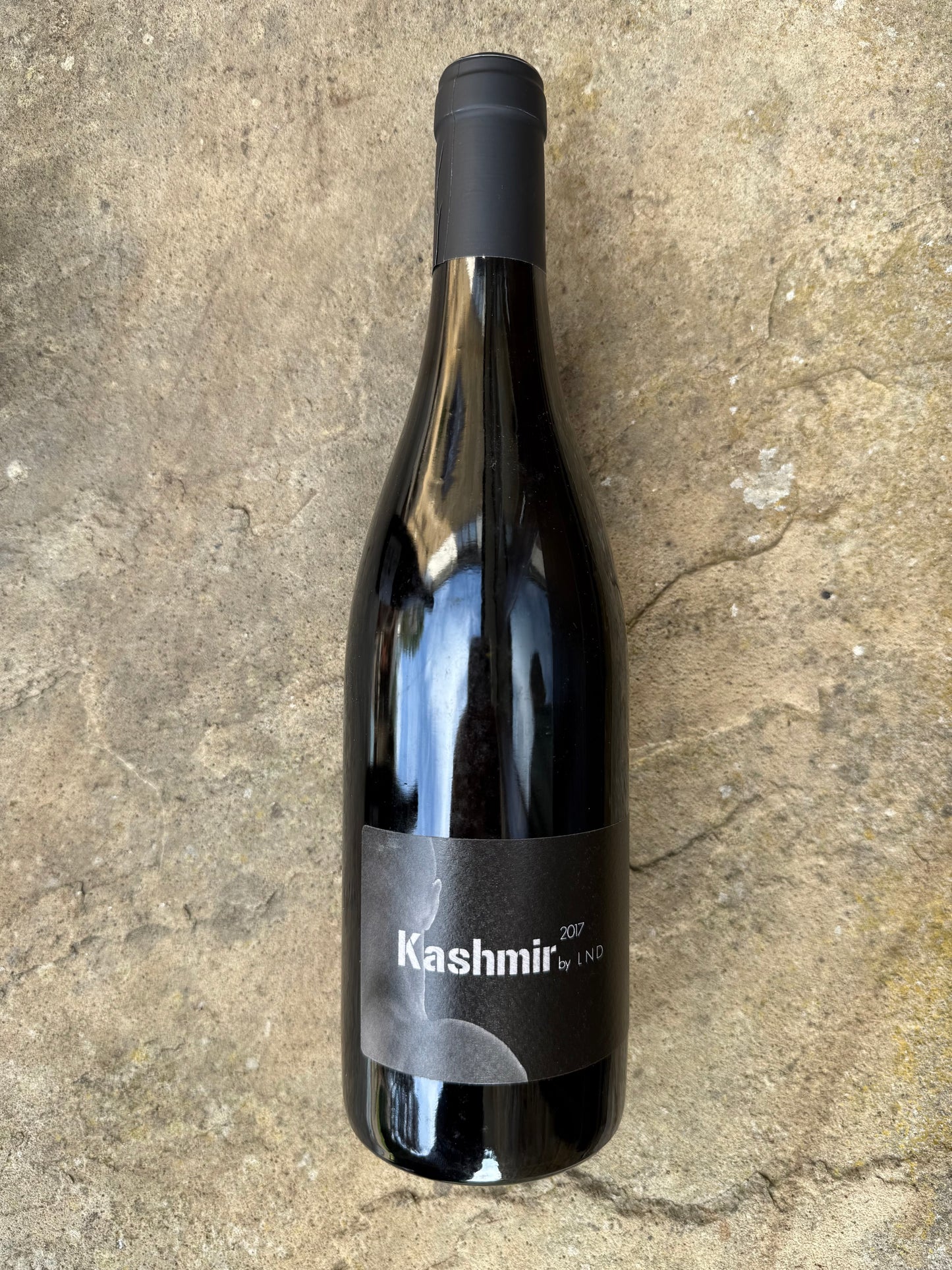 Bottle of Kashmir 2017 by La Nouvelle Don(n)e, a natural red wine with a bold label, photographed on stone—aged, organic, and perfect for BBQ pairings.