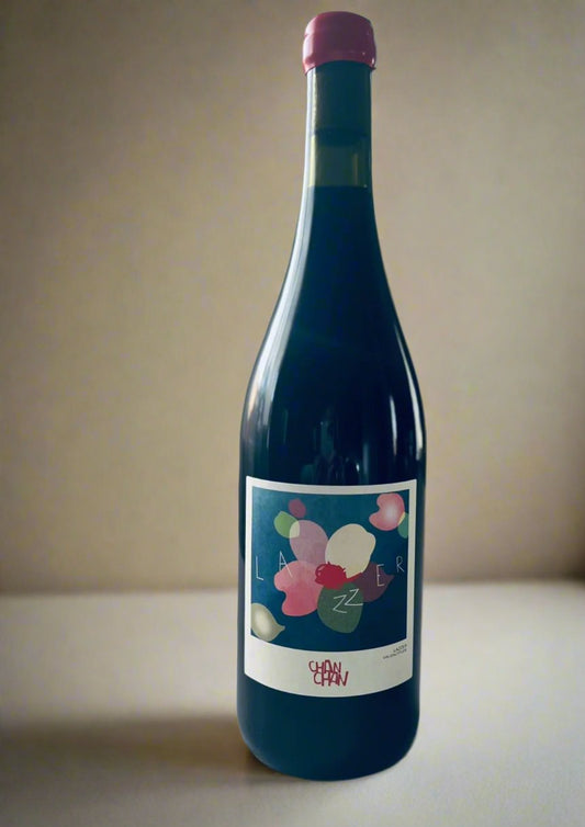 A bottle of Chan Chan Lazzer biodynamic red wine with a modern, artistic label featuring colourful abstract shapes. The wine is placed on a white surface with a soft gradient background.