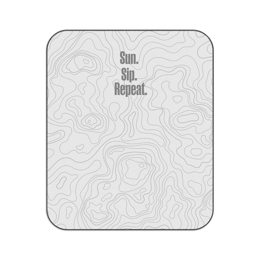Light grey picnic blanket with a minimalist topographic pattern and the phrase 'Sun. Sip. Repeat.' printed in bold grey text at the top left corner.